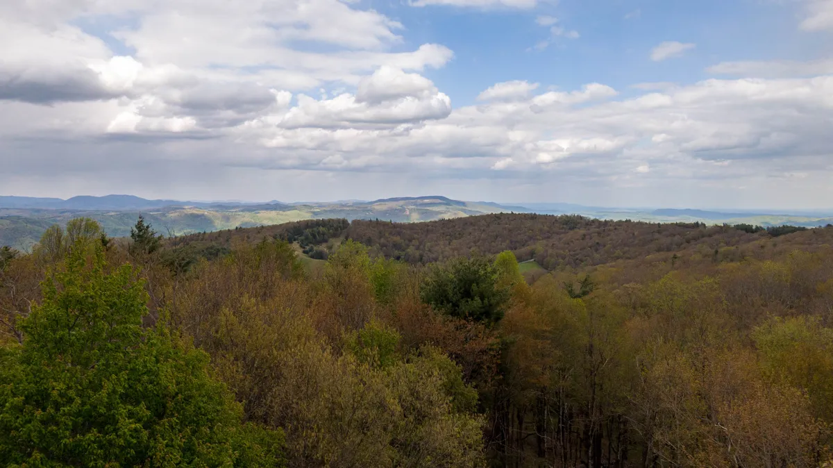 A sweeping view of the valley below, showcasing a vast mountain range, lush green trees, and a sprawling valley. The perspective hints at the elevated position of the property and the serene natural world that surrounds it, ideal for hiking, wildlife watching, or simply admiring the view.