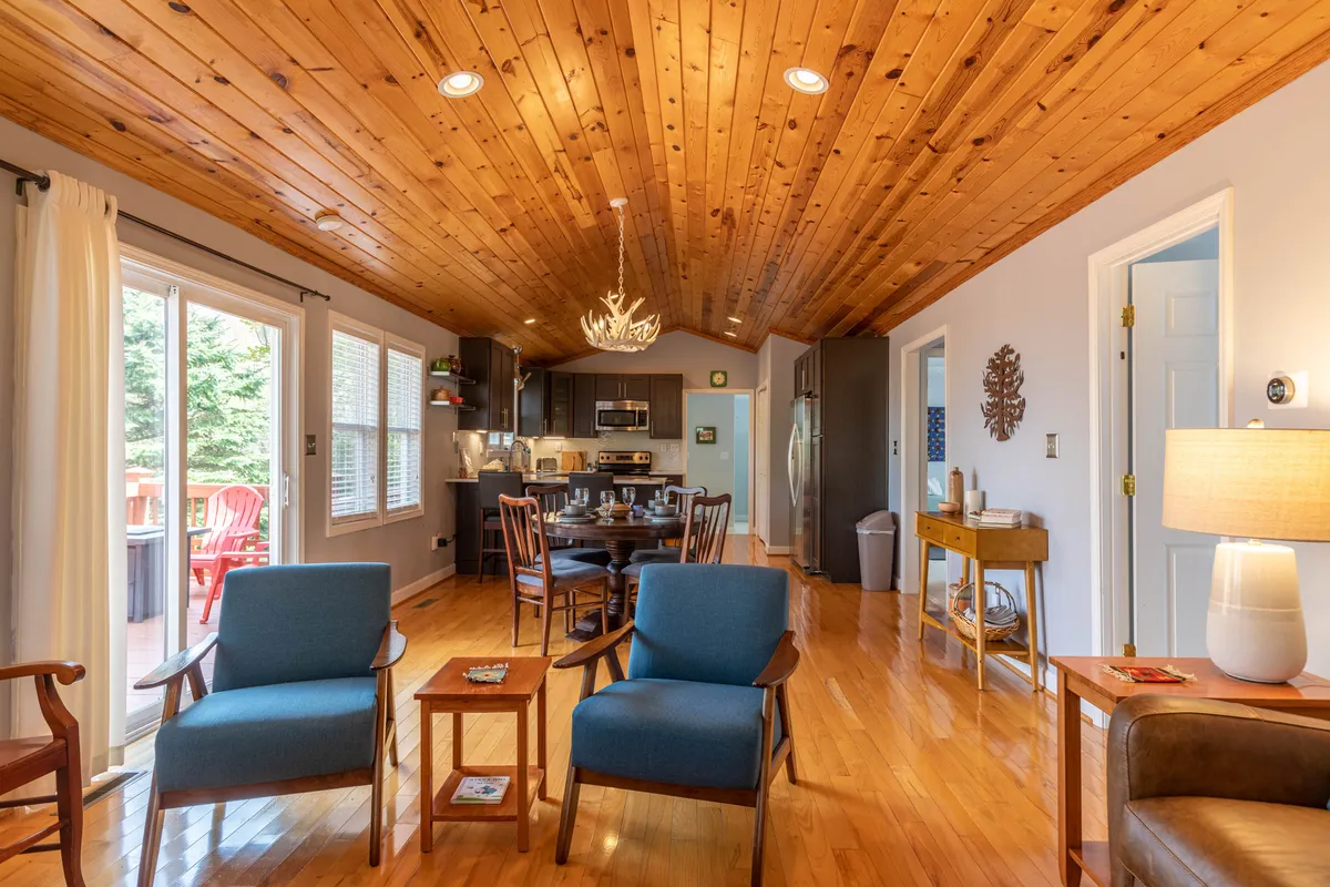A dining area beneath a striking wooden ceiling, featuring a sturdy wooden table surrounded by blue chairs and lit by a decorative lamp. The setting feels comfortable and casual—perfect for family gatherings or sharing casual meals, with hints of natural light that suggest scenic views beyond.