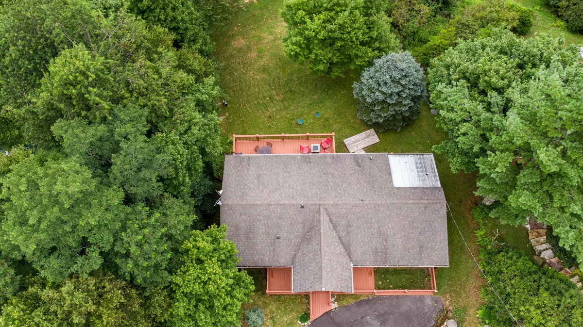 An inviting exterior shot of a residential home nestled in lush greenery, with a deck area that hints at opportunities for outdoor relaxation and enjoying the crisp mountain air.