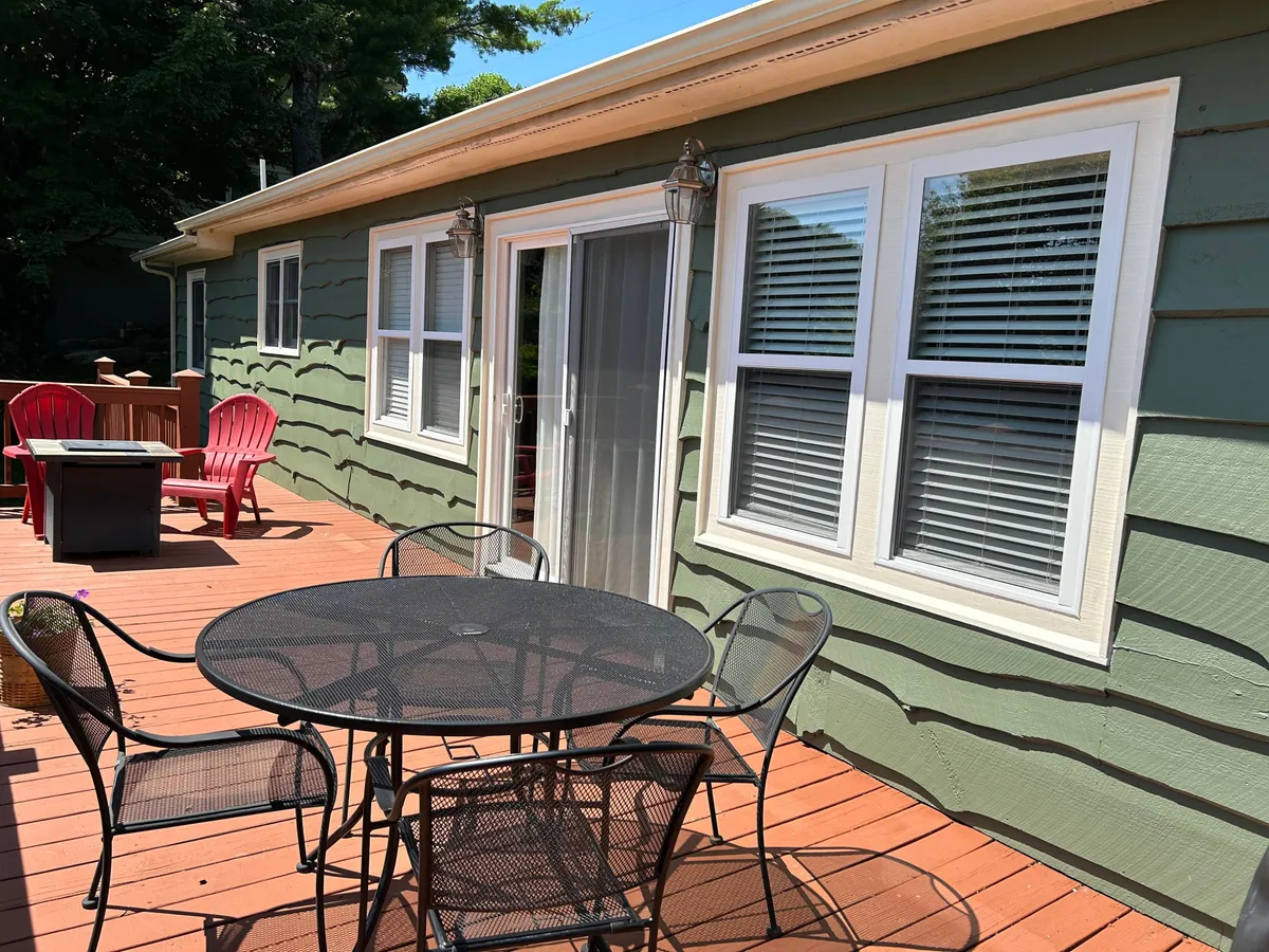 A comfortable exterior deck setup with red chairs and a black table, positioned for outdoor dining or relaxing. The sliding glass door connects the deck to the interior, and the space is clearly designed for gathering, enjoying meals, or savoring mountain air.