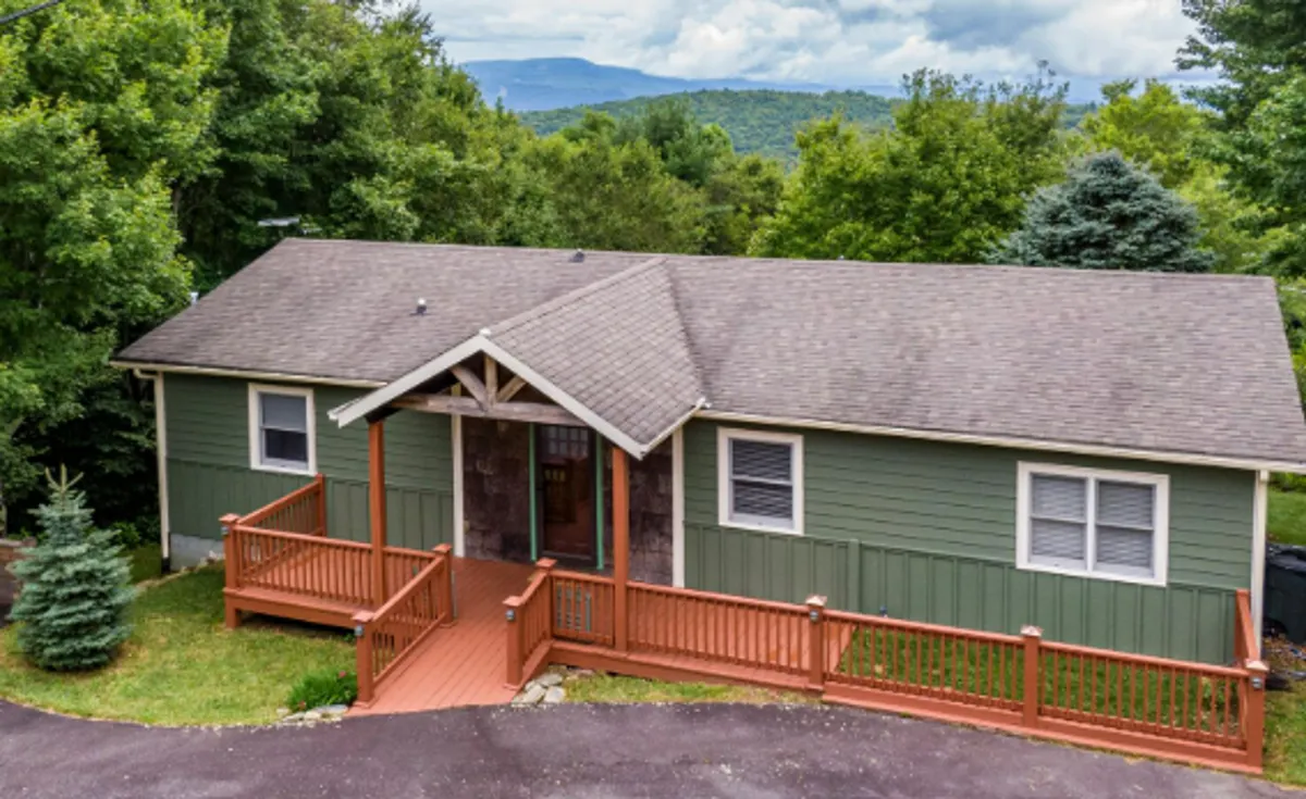 The hero image features a welcoming wooden deck attached to a green cabin, surrounded by lush trees. The elevated deck offers expansive views of the mountain landscape, inviting guests to relax outdoors, enjoy sunsets or morning coffee, and experience the tranquility of nature.