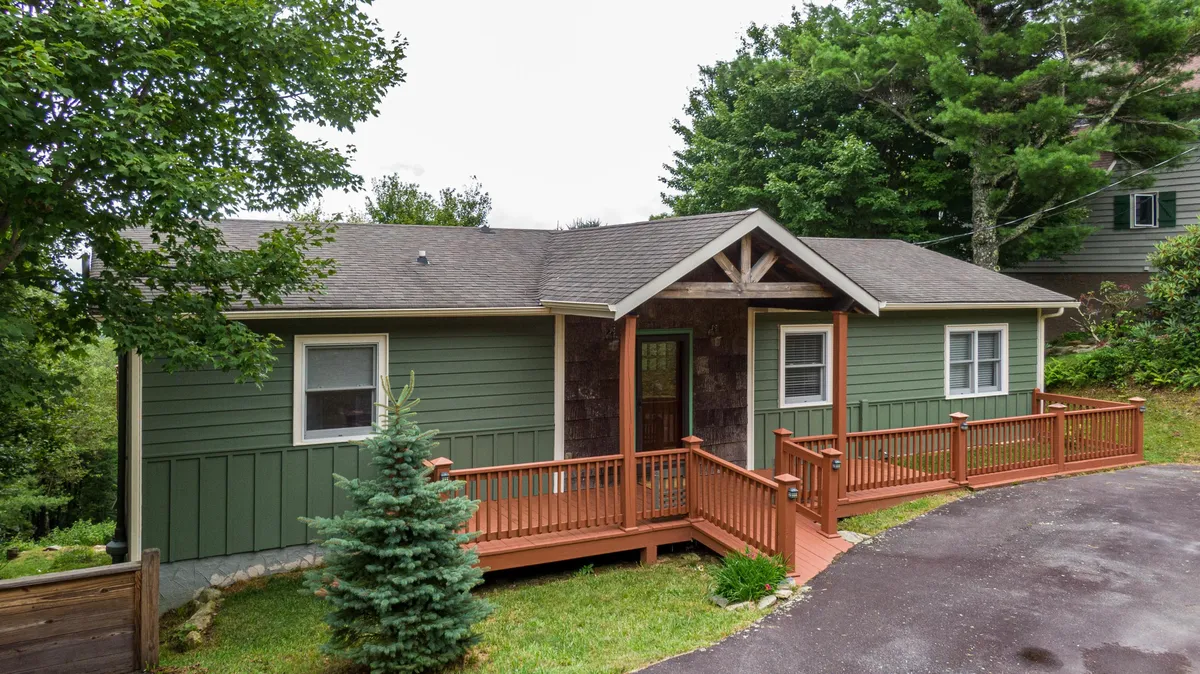 This image showcases the welcoming wooden deck and front entrance of the property, surrounded by lush greenery and stone accents. The deck area is spacious, inviting, and directly connects to the outdoors, hinting at a comfortable spot for both humans and their dogs to relax after a day of adventure.