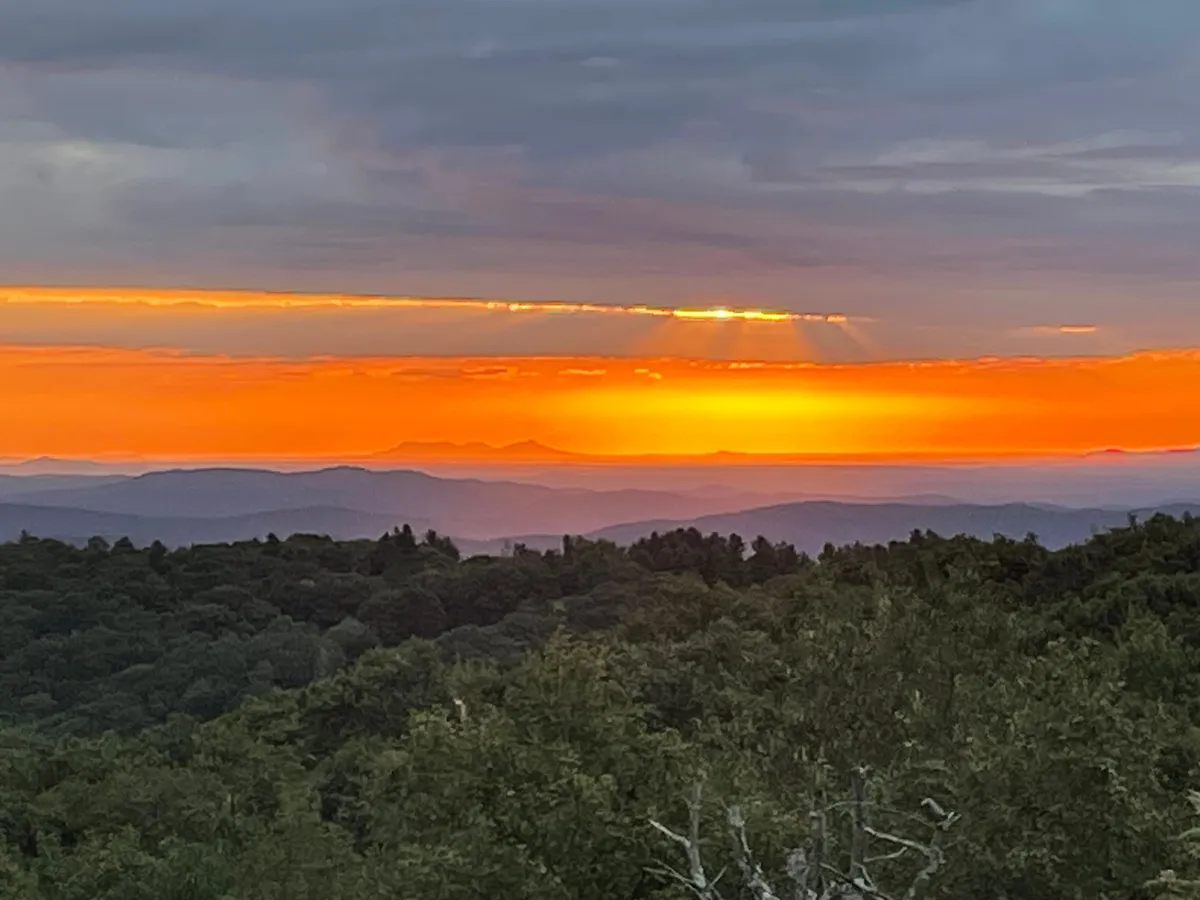A vibrant sunset paints the sky behind distant mountain silhouettes, with a lush green foreground suggesting healthy summer growth. The overall atmosphere is serene and inviting, ideal for outdoor adventures, relaxation, and soaking in nature’s tranquility.