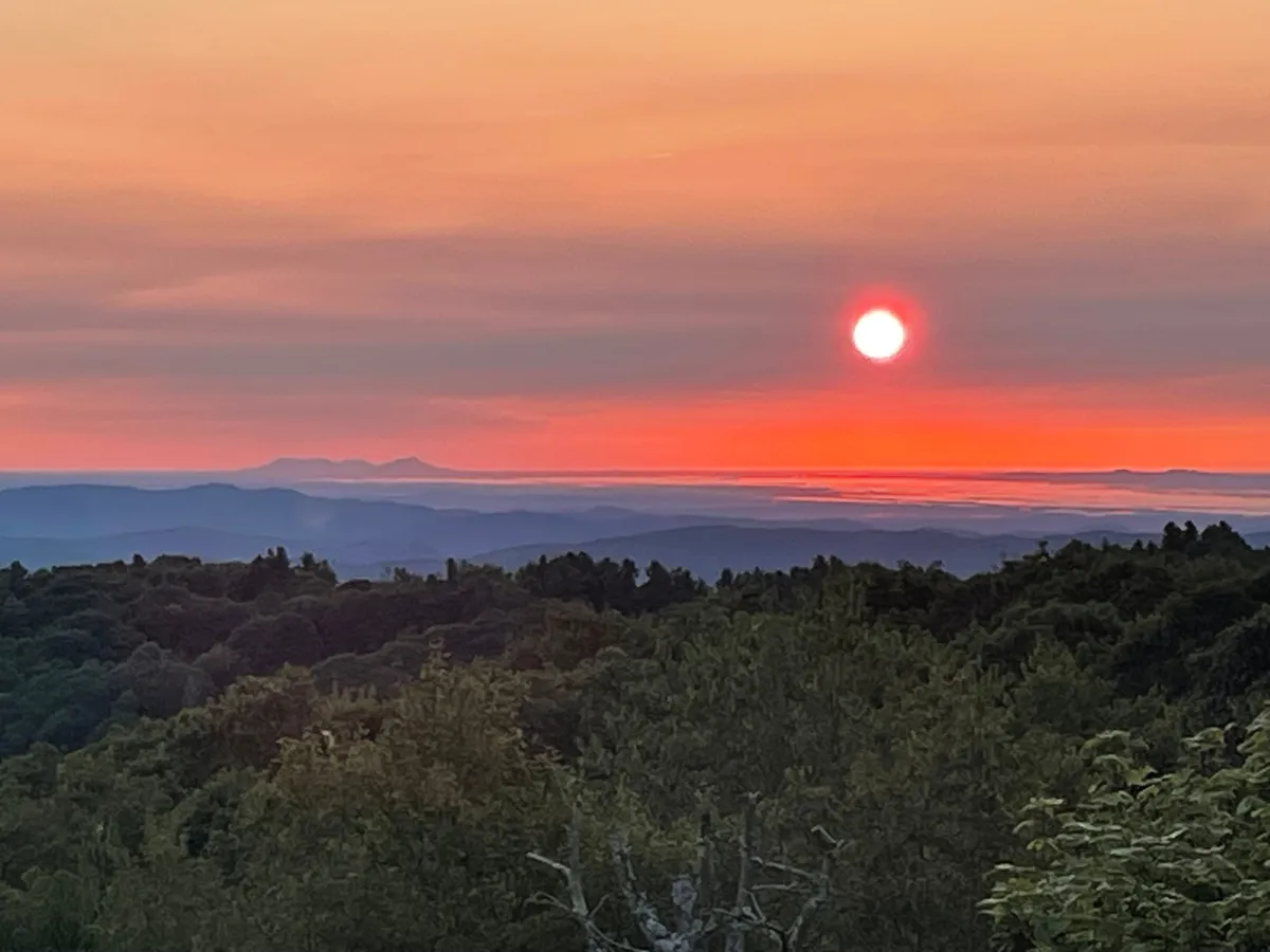 This image captures a stunning sunset over a mountain range, with the sky painted in warm, calming colors. The expansive view evokes a sense of serenity and wonder, reflecting the tranquility and beauty of a high elevation retreat.